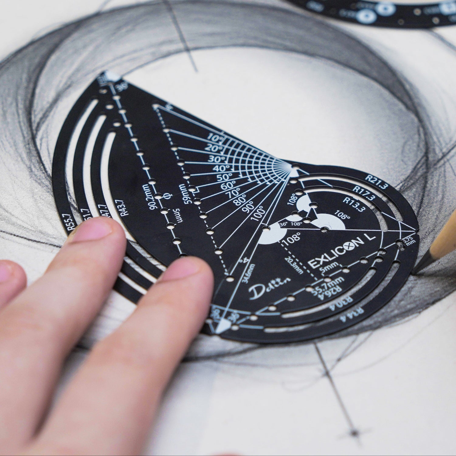 Person drawing intricate geometric designs on paper with a black golden ratio compass with measurement markings